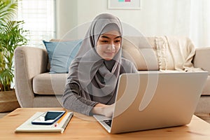 Muslim young women wear hijab using computer laptop typing work while sitting in the living room at home morning