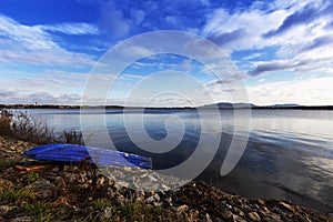 Musov lakes, fishing boat pulled out on a rocky shore of a lake with a calm reflection of the sky in the water at the setting sun.