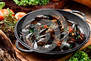 Mussel shells in vegetable broth in a black cauldron on a dark wooden background, decorated with vegetables