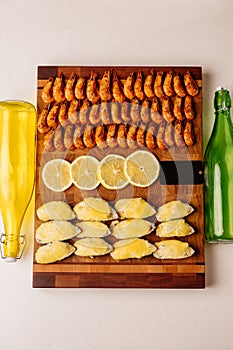 Mussels baked with cheese sauce and sliced lemon and fried shrimps on wooden cutting board with card and glass bottles