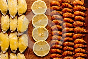 Mussels baked with cheese sauce and sliced lemon and fried shrimps on wooden cutting board close-up