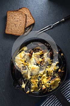 Mussels with cheese sauce in a frying pan, napkin and forks, bread