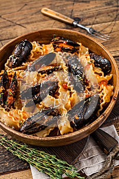 Mussels and clams Mafaldine pasta with tomato sauce in a rustic wooden plate. Wooden background. Top view