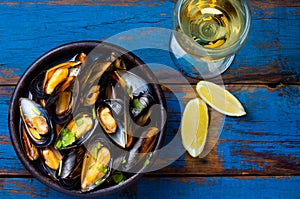 Mussels in clay bowl, glass of white wine and lemon