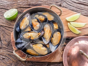 Mussels in copper pan on the wooden table.