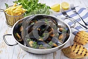 Mussels with french fries and herbs in cooking pan. White background. Close up