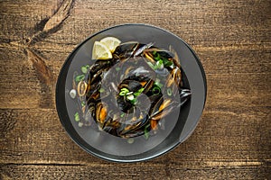 Mussels in garlic butter sauce served with lemon on wooden table