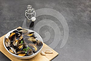 Mussels with open shells in white bowl on cutting board. Bottled water and sauce. Lemon and garlic