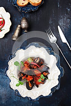 Mussels in tomato sauce with hot red pepper. Seafood on a plate. Stylish ceramic tableware. Vintage spice appliances. Close-up.Top