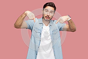 Must be here and right now. Portrait of serious handsome bearded young man in blue casual style shirt standing, pointing down and