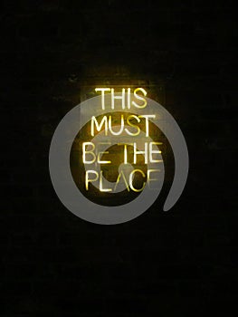 This Must Be The Place neon light sign on dark brick wall