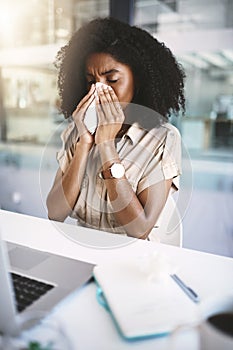 Must fight this flu. a young businesswoman blowing her nose with a tissue while working in a modern office.