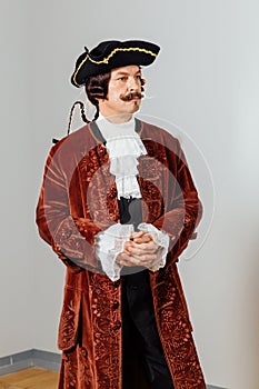 Mustachioed eccentric man in the vintage clothes of the baron. Hat tricorn, brown jacket.