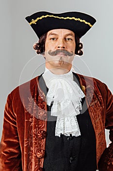 Mustachioed eccentric man in the vintage clothes of the baron. Hat tricorn, brown jacket.