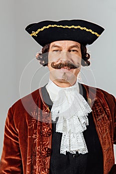 Mustachioed eccentric man in the vintage clothes of the baron. Hat tricorn, brown jacket.