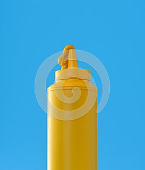 Mustard plastic bottle close up, minimalist on a blue background