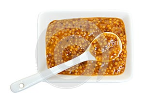 Mustard in a ramekin with a ceramic spoon, isolated against white background. Close-up, top view