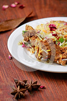 Mutton biryani on white plate dish on wooden table background garnish with rose petals and star anise close-up