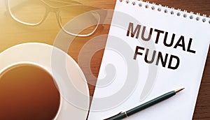 Mutual fund - text on paper with a cup of coffee and glasses on a wooden background in light. Business concept