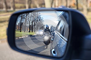 Mutual passing, motorcycle and vehicle with dazzle lighting overtaking the car, view in a side mirror. Improper driving or traffic photo