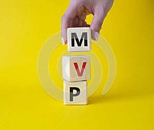 MVP - Most Valuable Player symbol. Wooden cubes with words MVP. Businessman hand. Beautiful yellow background. Business and MVP