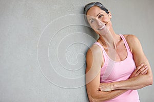 My body is feeling great. Portrait of an attractive mature woman in gymwear leaning against a gray wall.