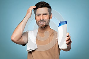 My choice. Handsome bearded man ready to take shower, standing with towel on shoulder, focus on bottle