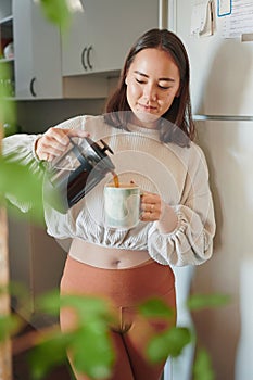 My day doesnt start until the coffee hits. a young woman pouring herself a cup of coffee.