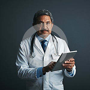 My digital doctoring assistant. Studio shot of a mature doctor using a digital tablet against a gray background.