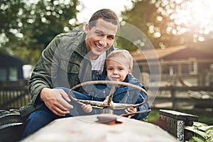 My duty as a Dad is to keep him smiling. Portrait of a father and his little son playing together on a farm tractor