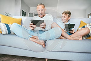 My father funs from PC games just like me.Father and son emotionally playing with electronic devices : tablet and gamepad sitting photo