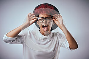 Are my glasses deceiving me. Studio shot of an attractive young woman screaming against a gray background.