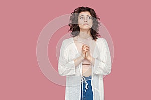 My God please help me. Portrait of worried hopeful beautiful brunette young woman with curly hairstyle in casual style standing,