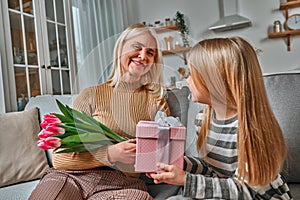 My grandmother is the best in the world! The little granddaughter gives her grandmother a gift and a bouquet of pink tulips.