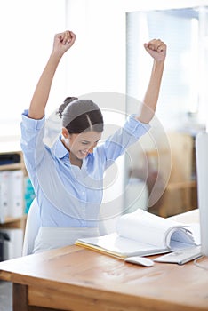 My hard work paid off. A young businesswoman celebrating a victory while sitting at her office desk.