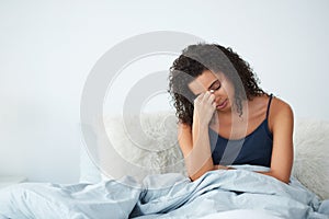 My head hurts just a little bit. an attractive young woman suffering from a headache and sitting in bed pinching her