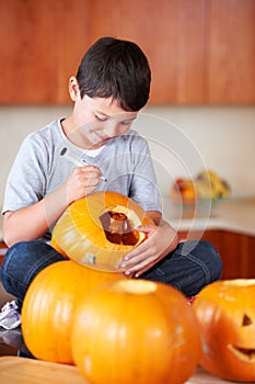 My Jack-O-Lantern is going to be the best. A little boy sitting cross-legged and drawing a face on a Jack Olantern.