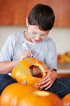 My Jack-O-Lantern is going to be the best. A little boy sitting in the kitchen making a Jack Olantern for Halloween.
