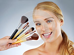 My little beauty boosters. Studio portrait of a beautiful young woman posing with makeup brushes against a grey