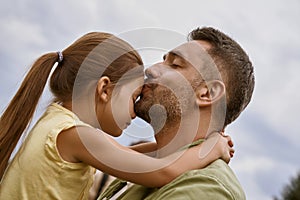 My little girl. Young loving father kissing his cute daughter in forehead while spending time together outdoors, blue