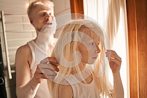 Girl standing at the bathroom and waiting while her father making braids for her