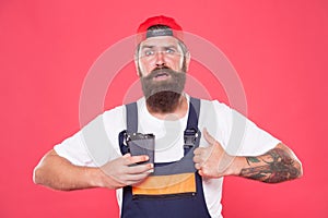 My morning coffee. serious brutal hipster with thumb up gesture. Portrait of man in uniform with coffee to go on red