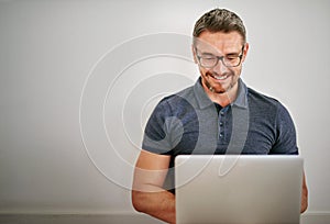 My post already has 100 likes. a man using his laptop while sitting against a gray wall.