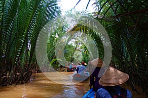 My Tho, Vietnam: Tourist at Mekong River Delta jungle cruise with unidentified craftman and fisherman rowing boats on flooding mud