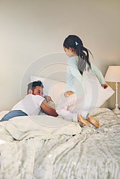 My turn to tickle you back. Shot of a cheerful little girl jumping on the bed to wakeup her sleeping dad at home.