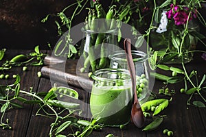 My veggie summer: peeled juicy fresh sweet green peas in glass jar, for making vegetable soup puree, dark wooden kitchen table