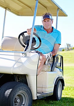 On my way to the next hole. A mature man driving a golf cart across the course.