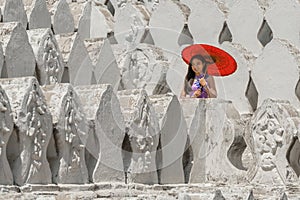 Myanmar woman with red umbrella in burmese traditional dress standing at Maha Sandar Mahi or Muni; Pagoda in Amarapura Mandalay