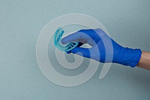 Myofunctional trainer for correction of bite and alignment of teeth in the hand of doctor in the glove  on blue background