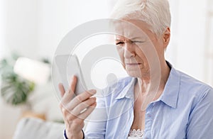 Myopia Concept. Elderly woman squinting while looking at smartphone screen